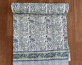 Könnte beinhalten: Eine weiße Baumwolldecke mit einem blauen und grünen Blumenmuster. Die Decke ist aufgerollt und hat einen Rand mit einem Paisley-Muster.
