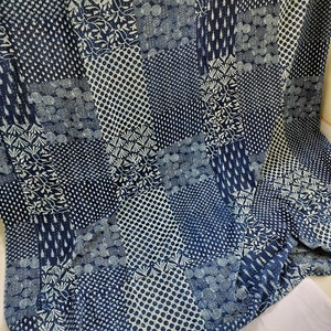 Op de afbeelding: Een blauwe en witte katoenen stof met een patchwork-ontwerp. De stof heeft verschillende patronen, waaronder cirkels, stippen en bloemmotieven.
