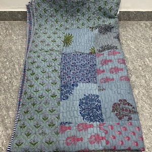 May include: A patchwork quilt featuring floral and lobster motifs in blue, green, and pink hues. The quilt has a striped border and is made of quilted fabric. The design combines diverse patterns and colours, suitable for a bed or sofa.