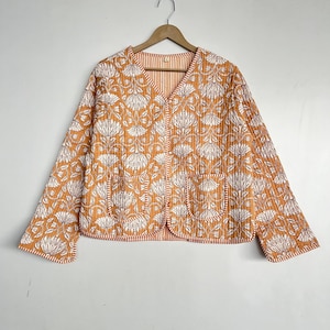 May include: A quilted jacket with a floral print in shades of orange and white. The jacket has a V-neck, long sleeves, and two pockets.