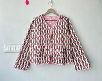 May include: A white jacket with a pink floral pattern and green leaves, featuring two front pockets and a pink trim. The jacket is hanging on a wooden hanger against a white wall.
