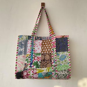 May include: A patchwork tote bag with a variety of floral and geometric patterns in shades of blue, green, pink, and brown. The bag has a white background and is trimmed with pink and green stripes.