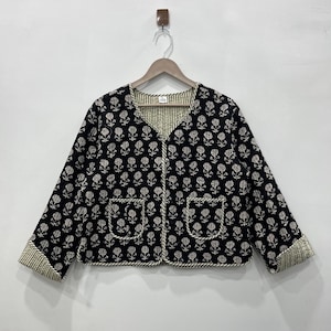 May include: A black quilted jacket with a white floral print and white trim. The jacket has a V-neck and two pockets.