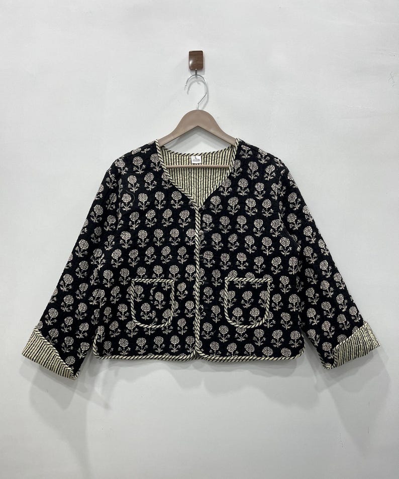 May include: A black quilted jacket with a white floral print and white trim. The jacket has a V-neck and two pockets.