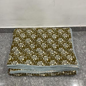 May include: Folded olive green quilt with a white floral pattern. The quilt has a striped border in shades of blue and white. The folded quilt is approximately 60 inches long and 40 inches wide.
