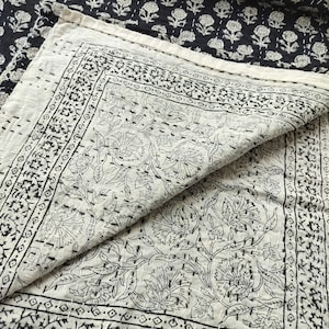 May include: A white cotton quilt with a black floral pattern. The quilt is folded in half, showing the intricate stitching and design.