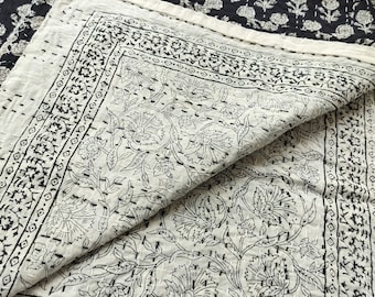May include: A white cotton quilt with a black floral pattern. The quilt is folded in half, showing the intricate stitching and design.