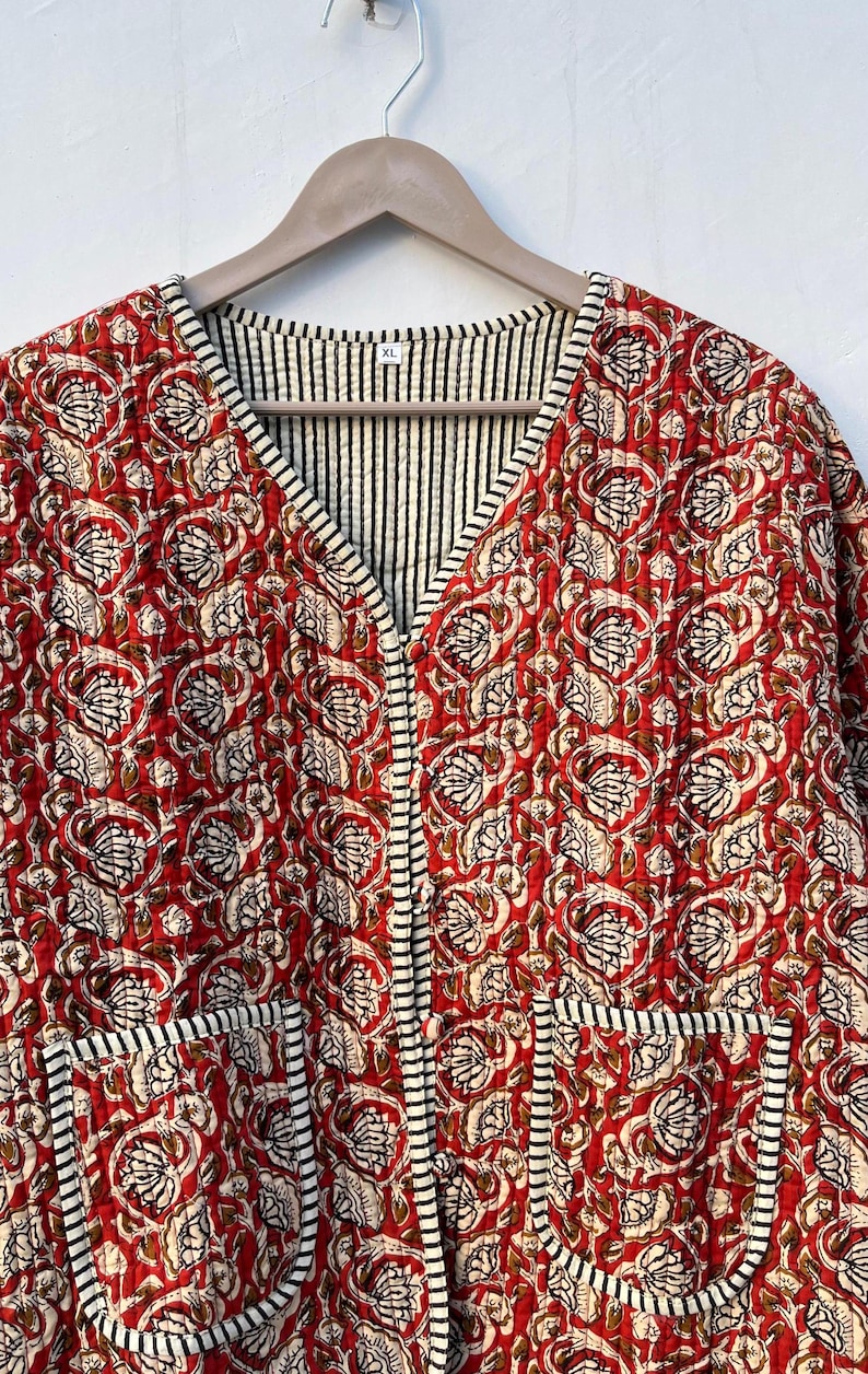 May include: A red quilted jacket with a floral print and black and white striped trim. The jacket has a V-neck and two pockets. The size tag says "XL".