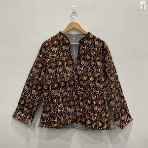 May include: A long-sleeved jacket with a floral pattern in brown, cream, and red on a black background. The jacket has a mandarin collar and a striped lining. It is hanging on a wooden hanger.