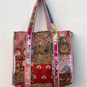 May include: A patchwork tote bag with pink, red, green, and brown fabric. The bag has a quilted design and a pink and white striped trim.