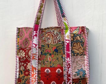 Può includere: Una borsa tote patchwork con tessuto rosa, rosso, verde e marrone. La borsa ha un design trapuntato e un bordo a righe rosa e bianco.