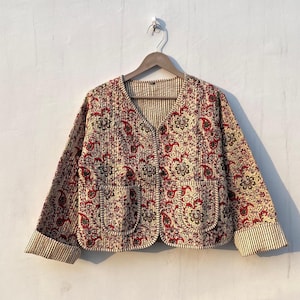 May include: A cream and red quilted jacket with a paisley print and a button closure. The jacket has a V-neck and long sleeves with striped cuffs.
