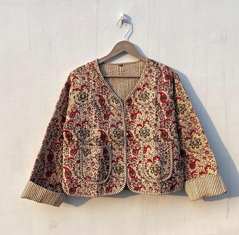 May include: A cream and red quilted jacket with a paisley print and a button closure. The jacket has a V-neck and long sleeves with striped cuffs.
