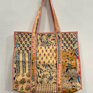May include: A patchwork tote bag with a variety of floral and geometric patterns in shades of yellow, blue, and pink. The bag has red and white striped trim and matching handles. The bag is made of a woven fabric.