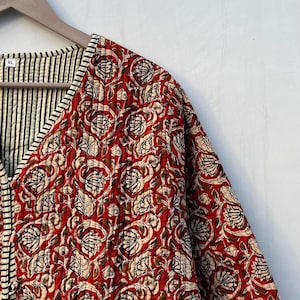 May include: A red and white floral quilted jacket with a black and white striped trim. The jacket has a V-neck and a button closure. The size tag says "XL".