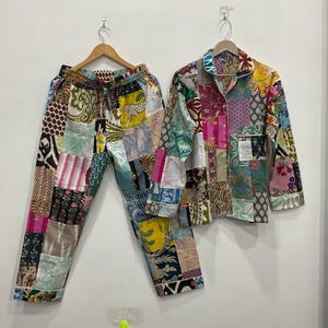 May include: A patchwork pajama set comprising a button-down shirt and matching trousers. The set is made from various fabric patterns in shades of pink, green, yellow, and blue. The trousers have a drawstring waist. The set is hanging on wooden hangers.