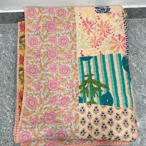 May include: A patchwork quilt with floral and striped patterns in pink, blue, and cream. The quilt features a variety of designs, including large pink flowers, teal stripes, and small blue floral motifs. The edges are finished with a red and white striped border.