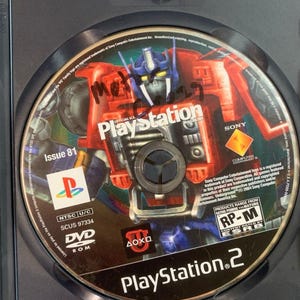 May include: A PlayStation 2 game disc for Official U.S. PlayStation Magazine Issue 81, featuring a red and blue robot graphic. The disc includes the PlayStation logo, Sony Computer Entertainment branding, ESRB RP-M rating, and text reading SCUS 97334.