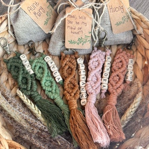 May include: A collection of six personalized keychains with tassels. Each keychain features a different name spelled out with wooden beads and is made with a macrame style cord. The keychains are displayed in a woven basket with small fabric bags.