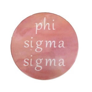 May include: A round, pink and white,  watercolor-style coaster with the text "phi sigma sigma" in white lettering.