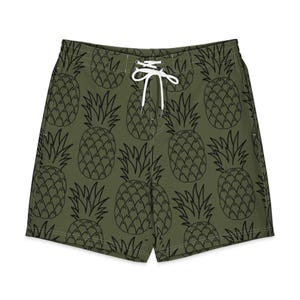 May include: Olive green swim trunks with a black pineapple pattern. The trunks have a white drawstring closure at the waist. The shorts are made of a lightweight material, perfect for the beach or pool.