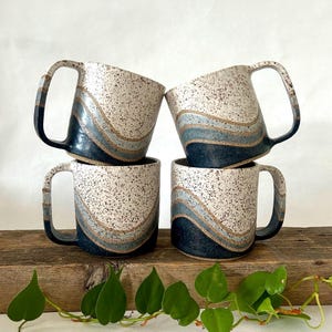 May include: Set of four ceramic mugs with a speckled white glaze and blue and brown wavy designs.
