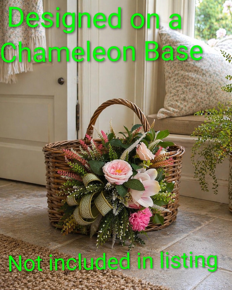 K&ouml;nnte beinhalten: Ein geflochtener brauner Weidenkorb mit einem dekorativen Arrangement aus rosa Rosen, wei&szlig;en Blumen, gr&uuml;nem Blattwerk und einem strukturierten olivgr&uuml;nen Band. Der Text "Designed on a Chameleon Base" und "Not included in listing" ist in leuchtendem Gr&uuml;n &uuml;berlagert.