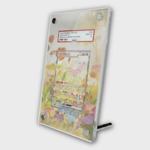 May include: A framed Pokémon trading card featuring a pink Mew character. The card is graded and encased in a clear acrylic display with a floral background. The card is labeled "2023 Pokemon Mew EN Blastose ex Special Illustration Rare".