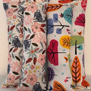 May include: Four rectangular fabric pillows with colorful floral and forest-themed patterns. The pillows feature designs with pink flowers, gray animals, and trees with red, orange, and yellow leaves. The background is a light gray.