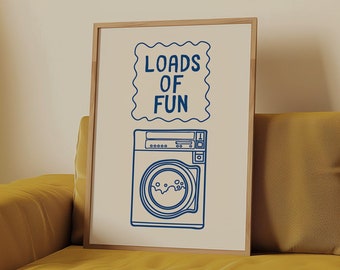 Op de afbeelding: Een ingelijst print met een blauwe illustratie van een wasmachine en de tekst "Loads of Fun" in een decoratief lettertype.