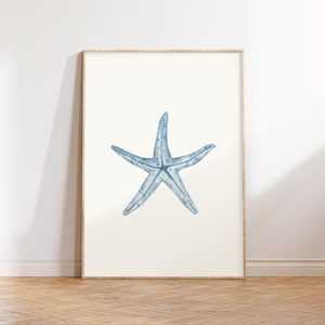 Puede incluir: Una ilustración de estrella de mar azul en acuarela sobre un fondo blanco. La estrella de mar está en el centro de la imagen y está mirando al espectador.