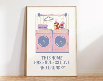 Op de afbeelding: Een ingelijst print met een roze en witte illustratie van twee wasmachines, wasmiddelflessen en een hanger. De tekst "This home has endless love and laundry" is onder de illustratie gedrukt.