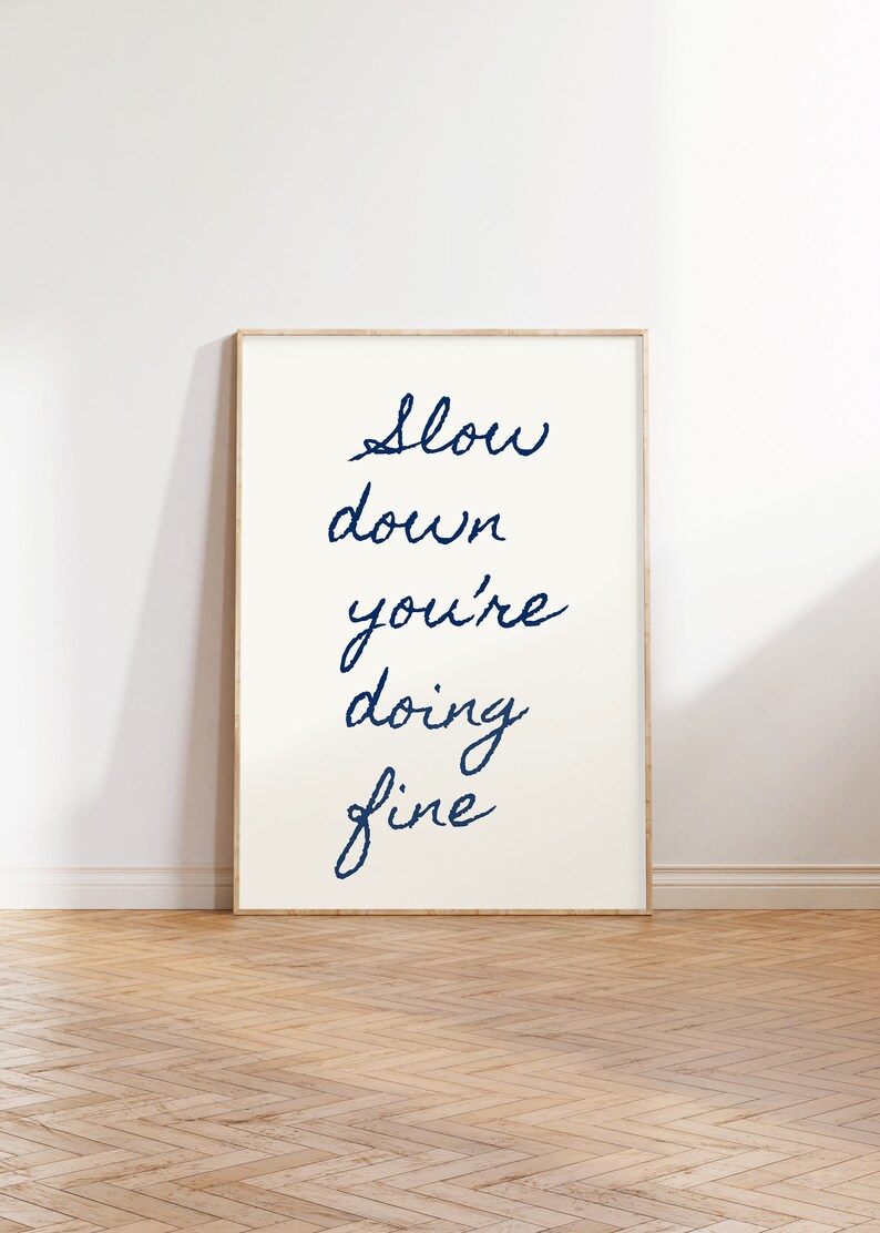 May include: A framed print with the text "Slow down you're doing fine" in blue cursive writing on a white background.