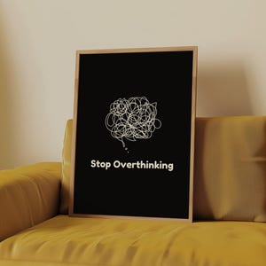 Pu&ograve; includere: Un poster nero incorniciato con un'illustrazione bianca di una bolla di pensiero aggrovigliata e il testo "Stop Overthinking" su un divano giallo.