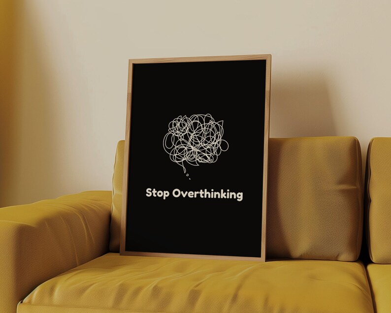 Pu&ograve; includere: Un poster nero incorniciato con un'illustrazione bianca di una bolla di pensiero aggrovigliata e il testo "Stop Overthinking" su un divano giallo.