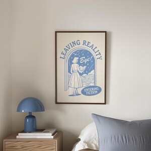 Puede incluir: Una impresi&oacute;n enmarcada azul y blanca con el texto "Leaving Reality Bye! Entering Fiction" y un dibujo de una mujer con un vestido caminando a trav&eacute;s de una puerta.