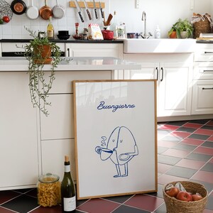 Peut inclure: Une impression encadr&eacute;e avec une illustration bleue d'un personnage de grain de caf&eacute; disant "Buongiorno" dans un cadre blanc sur un sol &agrave; carreaux noirs et rouges.