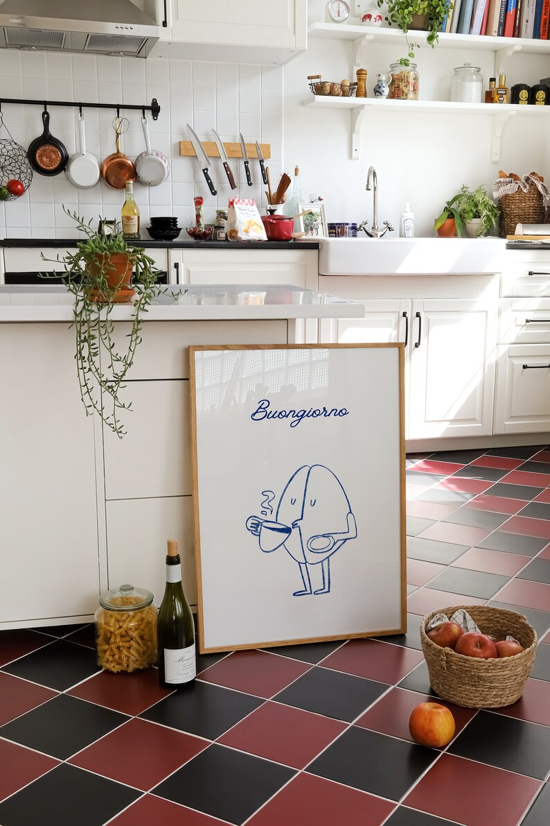 Peut inclure: Une impression encadr&eacute;e avec une illustration bleue d'un personnage de grain de caf&eacute; disant "Buongiorno" dans un cadre blanc sur un sol &agrave; carreaux noirs et rouges.
