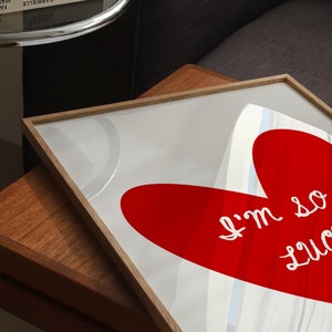 May include: A framed print with a red heart shape and the text "I'm so lucky" in white. The print is on a wooden table.