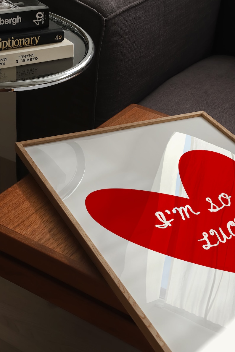 May include: A framed print with a red heart shape and the text "I'm so lucky" in white. The print is on a wooden table.