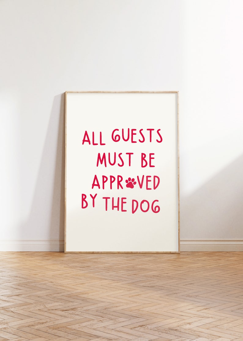 Puede incluir: Un cartel enmarcado blanco con el texto "ALL GUESTS MUST BE APPROVED BY THE DOG" en letras rojas con una huella de pata roja en la palabra "APPROVED".