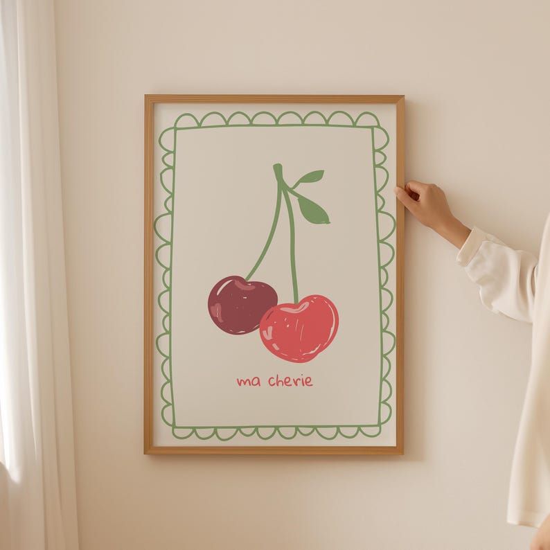 May include: A framed print with a green scalloped border. The print features a simple illustration of two red cherries with green stems and leaves. The text "ma ch&eacute;rie" is written below the cherries.