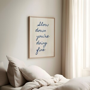 May include: A framed print with the text "Slow down you're doing fine" in blue cursive writing on a white background.