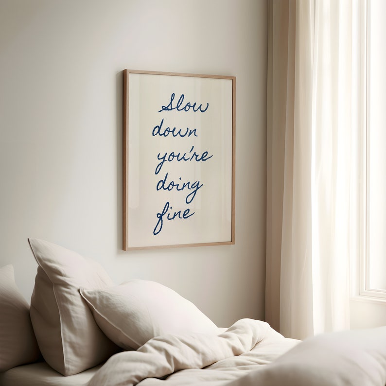 May include: A framed print with the text "Slow down you're doing fine" in blue cursive writing on a white background.