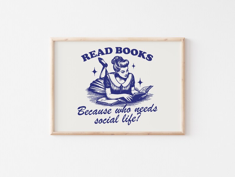May include: A framed print with a vintage navy blue illustration. It depicts a woman reading a book, with the text "READ BOOKS" above and "Because who needs social life?" below. The print is set in a light wood frame.
