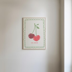 May include: A framed print with a green border and a white background. The print features a simple illustration of two red cherries with green stems and leaves. The text "ma cherie" is written below the cherries.