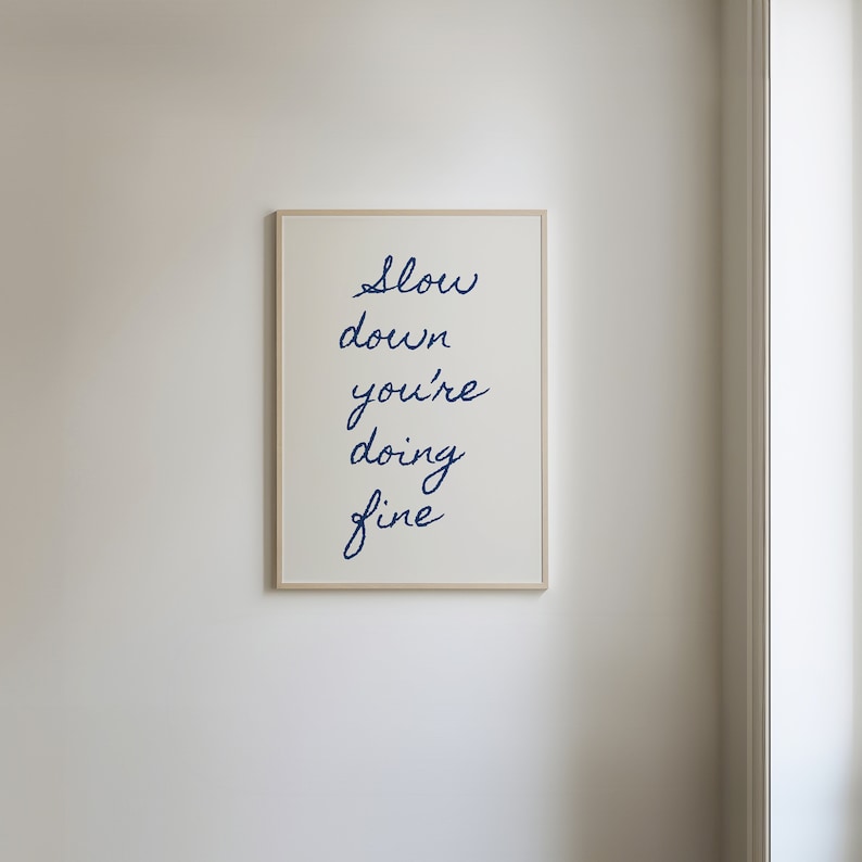 May include: A framed print with the text "Slow down you're doing fine" written in blue cursive script on a white background.
