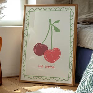May include: A framed print with a green border and a white background. The print features a simple line drawing of two red cherries with green stems and leaves. The text "ma ch&eacute;rie" is written below the cherries.