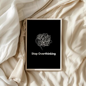 Pu&ograve; includere: Una stampa incorniciata nera con un disegno a linea bianca di una bolla di pensiero aggrovigliata e il testo "Stop Overthinking" su uno sfondo di tessuto beige.