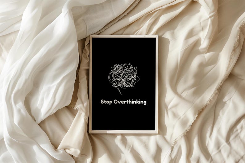 Pu&ograve; includere: Una stampa incorniciata nera con un disegno a linea bianca di una bolla di pensiero aggrovigliata e il testo "Stop Overthinking" su uno sfondo di tessuto beige.